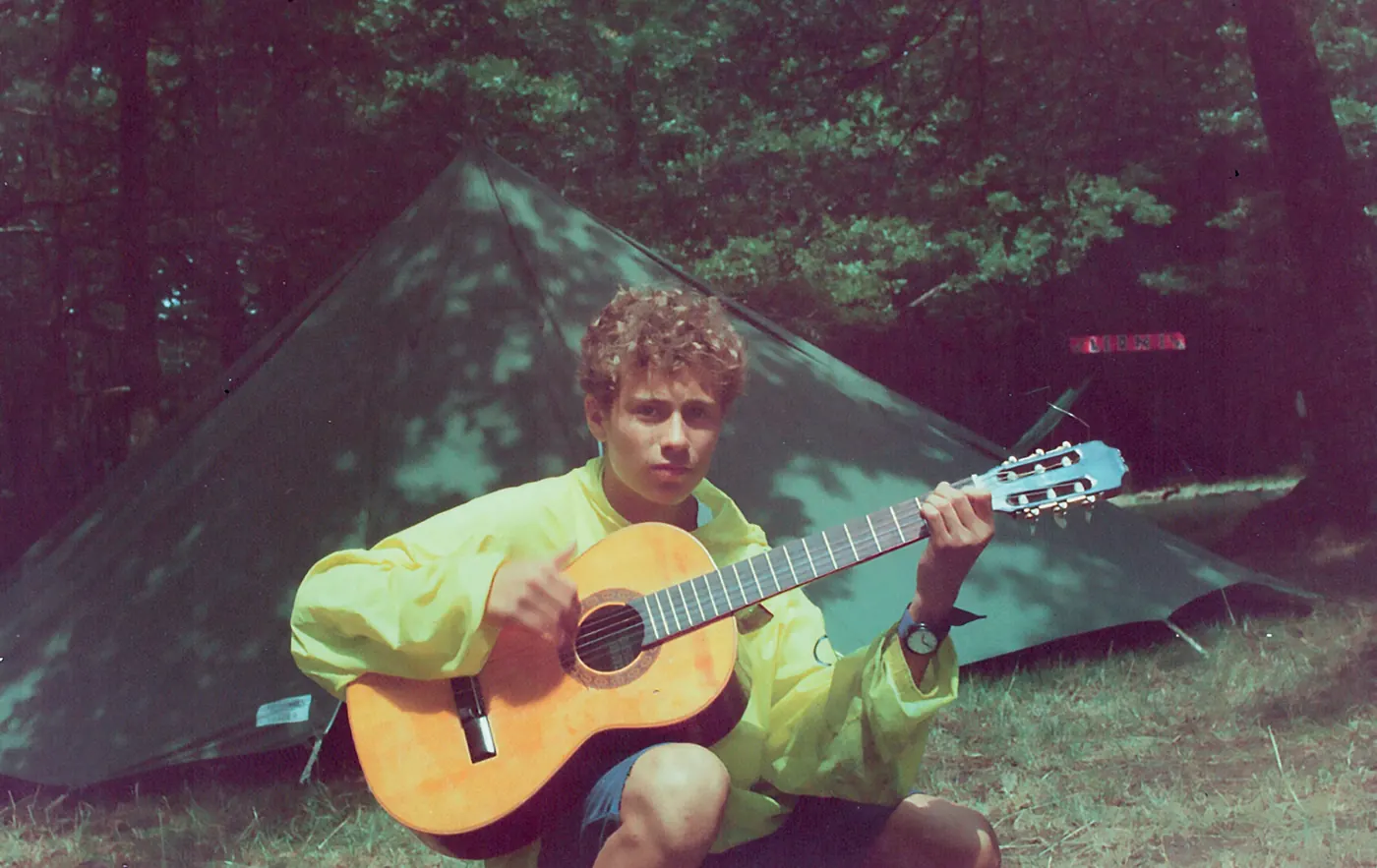 Un ragazzo suona la chitarra davanti a una tenda